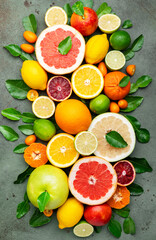 Colorful citrus fruits, food background, top view. Mix of different whole and sliced fruits: orange, grapefruit, lemon, lime and other with leaves on  green stone table