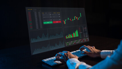 Caucasian man sits in the dark in front of a virtual screen. Stock exchange charts. Close-up of male hands on the keyboard.