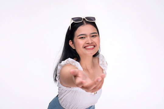 A young asian woman extends her hand offering her help. A selfless lady warmly smiling being supportive. Isolated on a white background.