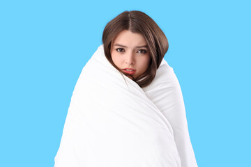 Sleepy young woman with soft blanket on blue background