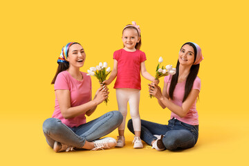 Young lesbian couple and adopted little girl with tulips on yellow background