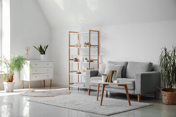 Interior of living room with sofa, houseplants and stylish holder for books on coffee table