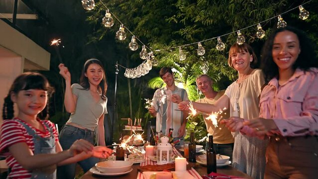 Family and friends gathering celebrating outdoor new year party and play festival sparklers together having enjoy at home. Big family multi-ethnic celebrating outdoors party at garden.