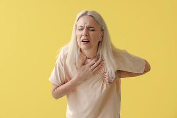 Mature woman having heart attack on yellow background