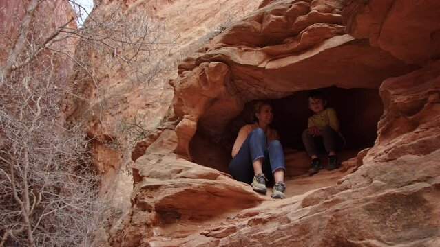 Woman and 5 year old son explore red rock cave in slot canyon, Escalante Utah