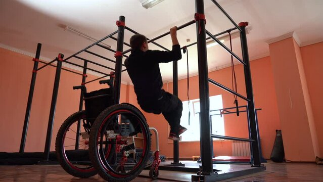 A young man in a wheelchair on a gymnastic pull-up bar in the gym performing exercises