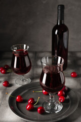 Glasses and bottle of sweet cherry liqueur with fresh berries on grey grunge table