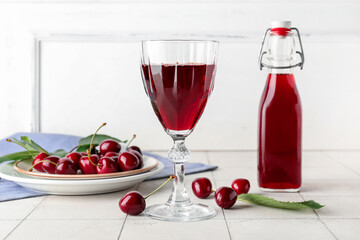 Glass and bottle of sweet cherry liqueur with berries on white tile table