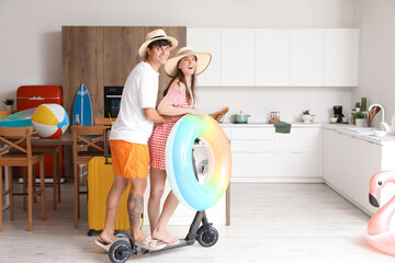Young couple with beach accessories ready for summer vacation in kitchen