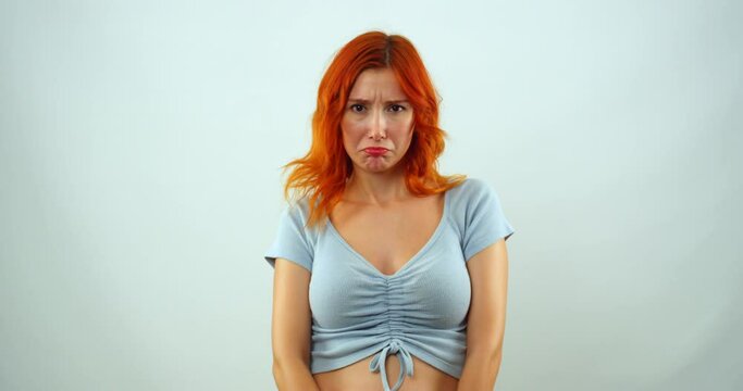 In a studio environment, a young girl looks at the camera and, in slow motion, shrugs her shoulders with a childish grumpiness and makes gestures that show that she is resentful
