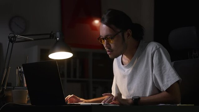 Asian man graphic designer working on computer drawing sketches logo design. Young Asian businessman looking serious and stressed while using laptop to work from home.