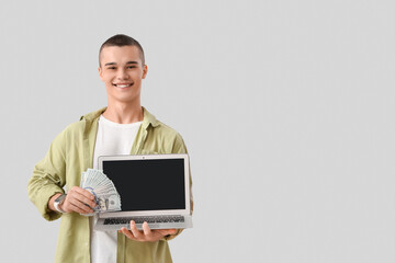 Young man with dollar banknotes and laptop on light background