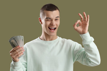 Young man with dollar banknotes showing OK on green background