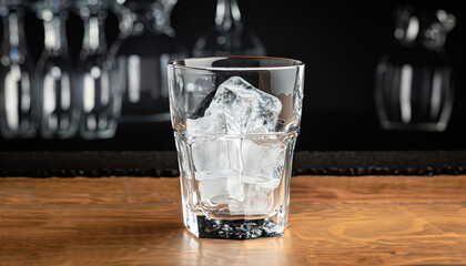 Ice cubes in an empty glass on a wooden bar counter, dark background, front view with details