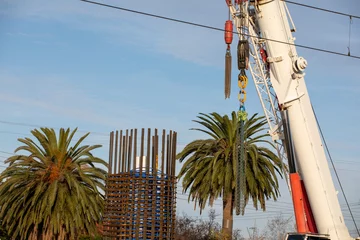 Tuinposter Reinforcing bars of a rail bridge footing under construction, with a crane boom and two palm trees. © Tanya Stawitzki