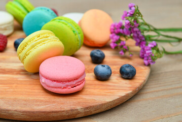 Board with sweet macaroons and blueberries on wooden background