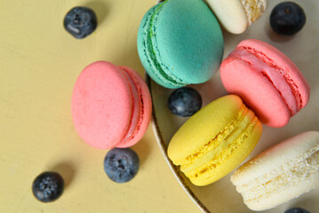 Plate with sweet macaroons and blueberries on yellow background