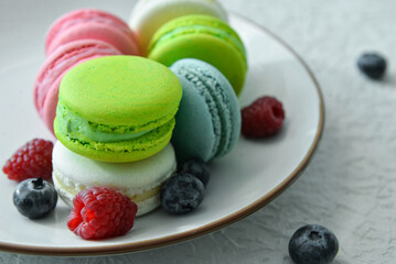 Plate with sweet macaroons and berries on light blue background