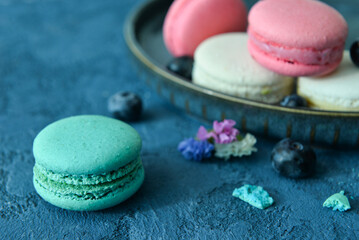 Plate with sweet macaroons and blueberries on blue background