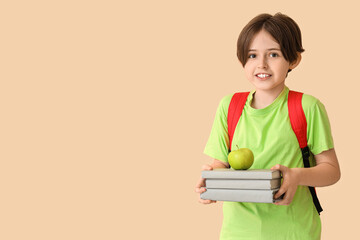 Happy little boy with backpack, books and apple on beige background