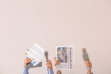 Female hands with newspapers and microphones on light background