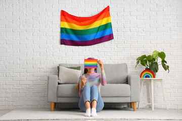Young woman with LGBT flag sitting on floor at home
