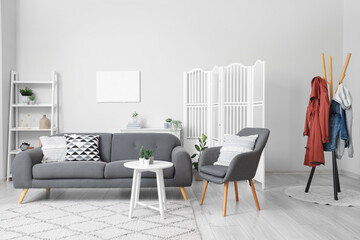 Interior of light living room with cozy armchair and grey sofa