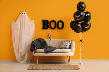 Different black Halloween balloons, sofa, ghost and text BOO hanging on orange wall in room
