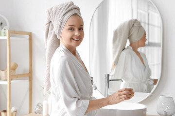 Young woman with cream after shower near mirror in bathroom