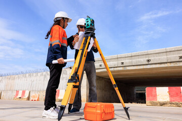 Engineer use theodolite equipment and looking blueprints construction project for route surveying to build a bridge across the intersection to reduce traffic congestion during rush hours