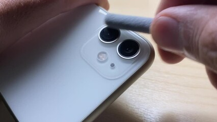Hand using small tool brush to clean dust and dirt from phone camera lens. Disinfecting mobile phone concept. Male hand holding smartphone close up view on wooden table - Powered by Adobe