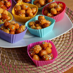 Traditional italian fried Struffoli with honey and sugar sprinkles on a plate on wooden table