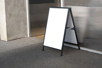 Side view of a blank white empty sandwich board placed at a half open door of a building entrance....