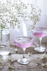 Pink cocktail placed on wooden board near the window with flowers as decoration. Great summer cocktail suggestion and party