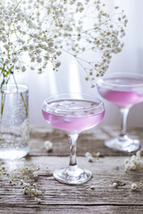 Pink cocktail placed on wooden board near the window with flowers as decoration. Great summer cocktail suggestion and party