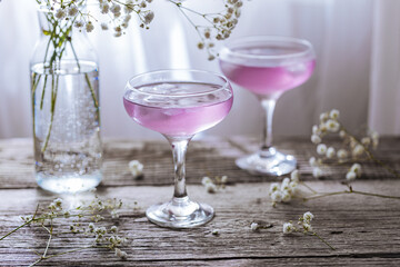 Pink cocktail placed on wooden board near the window with flowers as decoration. Great summer cocktail suggestion and party