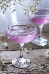 Pink cocktail placed on wooden board near the window with flowers as decoration. Great summer cocktail suggestion and party