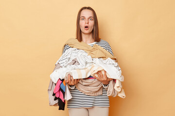Shocked astonished brunette woman isolated over beige background holding pile of dirty towels and...