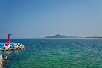 a landscape with a blue sea and a red lighthouse