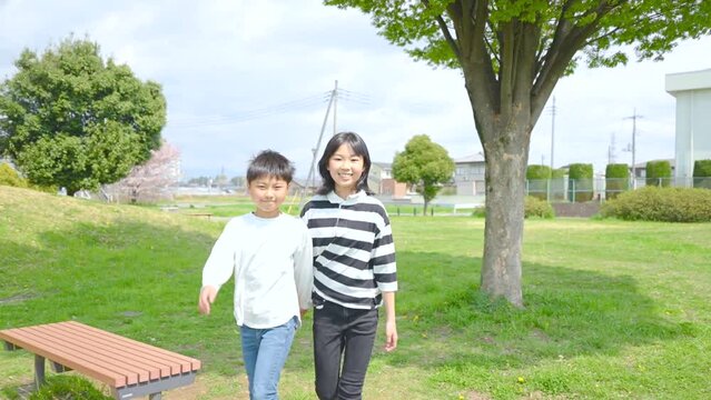 自然豊かな公園を歩くアジア人の姉と弟