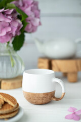 A cup of coffee, goodies, a teapot and flowers nearby