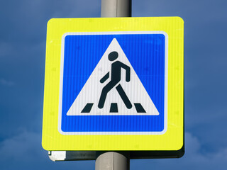 Close-up pedestrian crossing sign with bright yellow frame on cloudy dark blue sky background.