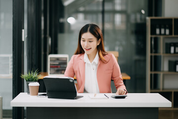 Successful Asian Businesswoman Analyzing Finance on Tablet and Laptop at modern Office Desk tax, report, accounting, statistics, and analytical research concept.