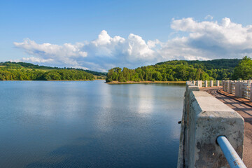 Crescent lake of a dam with road crossing water and forest-covered hill in the Morvan in France