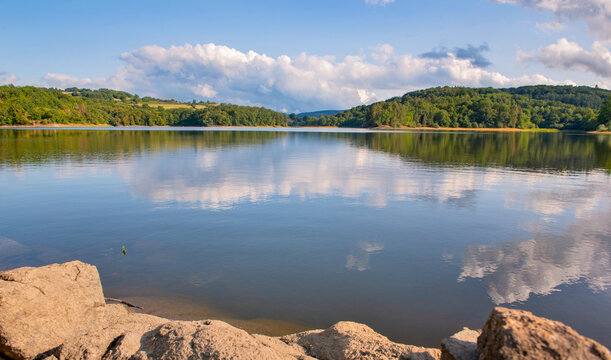 white clouds reflecting in the blue water of Crescent lake and forest-covered hill in the Morvan in France