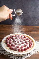 Round homemade raspberry cheesecake is decorated with powdered sugar