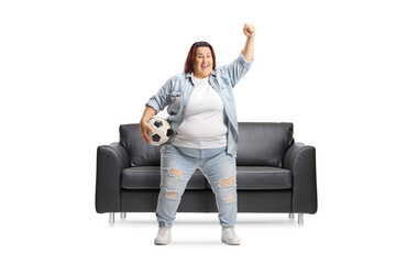 Overweight young woman cheering with a football in front of a black leather sofa