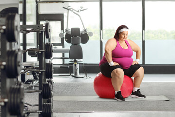 Young overweight woman sitting on a fintess ball at a gym