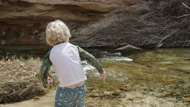Little 3 year old boy hurls large stone into stream in slow motion