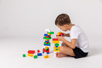 Toddler playing with educational blocks. Side view happy child collects a tower of colored cubes....